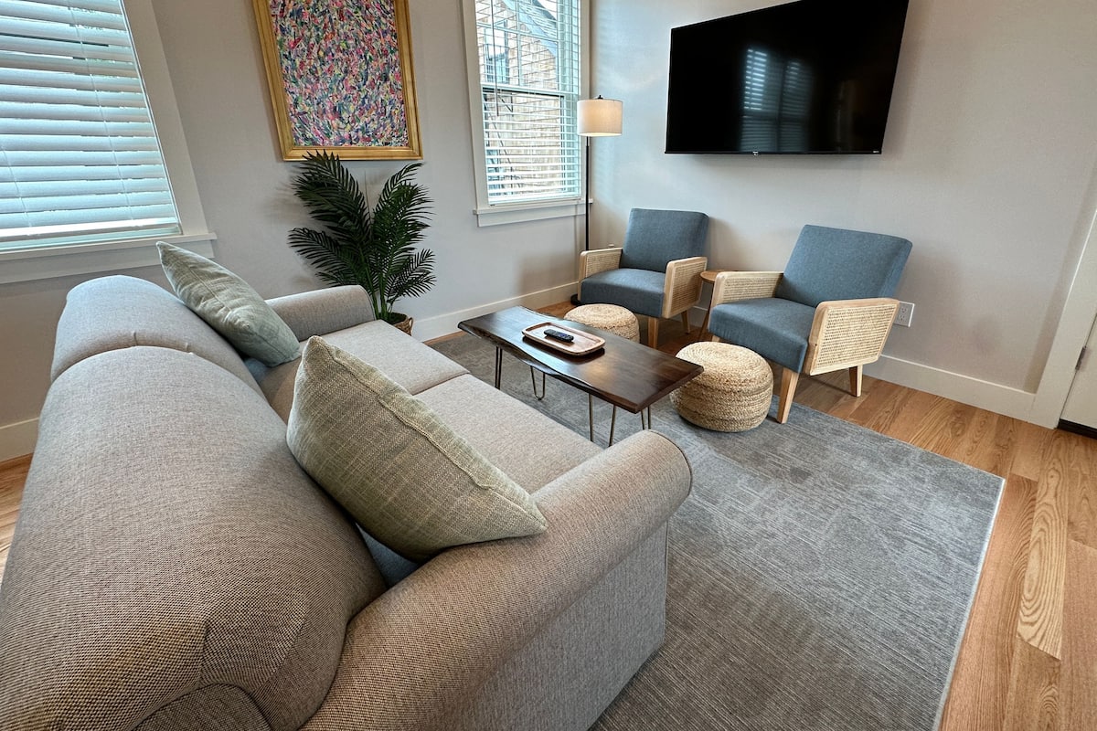 A modern living room with a grey sofa, blue armchairs, a coffee table, and a flat-screen TV mounted on the wall.