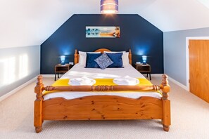 A bedroom with a wooden bed, two bedside tables, a nightstand, a wall-mounted lamp, and a door. - Stylish Margate Coastal Home Parking By Adliv (Margate)