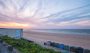 A beach with a clear sky and a sunset. There is a building with a sign, a fence, and some greenery in the foreground. - Stylish Margate Coastal Home Parking By Adliv (Margate)