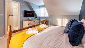 A bedroom with a bed, a TV mounted on the wall, a wooden dresser, and a door leading to another room. - Stylish Margate Coastal Home Parking By Adliv (Margate)