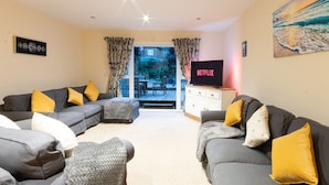A living room with two grey sofas, yellow cushions, a white cabinet, and a TV displaying 'NETFLIX'. - Stylish Margate Coastal Home Parking By Adliv (Margate)
