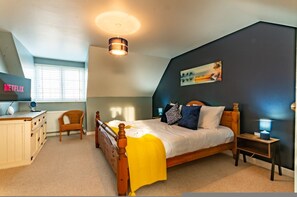 A bedroom with a bed, bedside tables, a chair, a desk with a computer, a lamp, and a painting on the wall. - Stylish Margate Coastal Home Parking By Adliv (Margate)