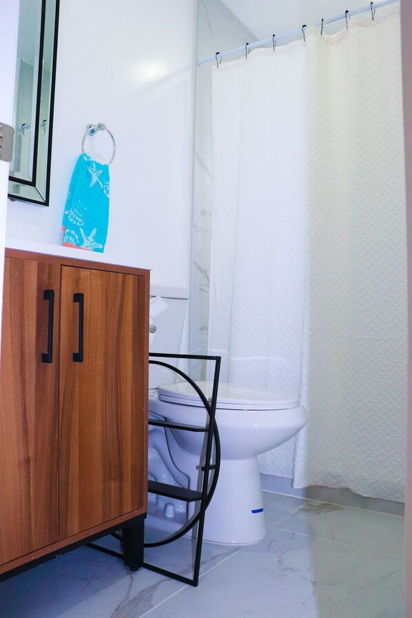 A bathroom with a wooden cabinet, a white toilet, and a shower curtain. - Flamingo Beach House (Dania Beach)