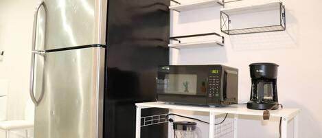 Cocina compacta con refrigerador de acero inoxidable, microondas y cafetera sobre una encimera blanca.
