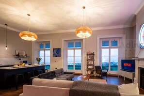 Un salon moderne avec un canapé, une table basse et un téléviseur. Il y a également un coin cuisine avec un bar et une table à manger. La pièce est dotée de grandes fenêtres et offre une vue sur la ville.