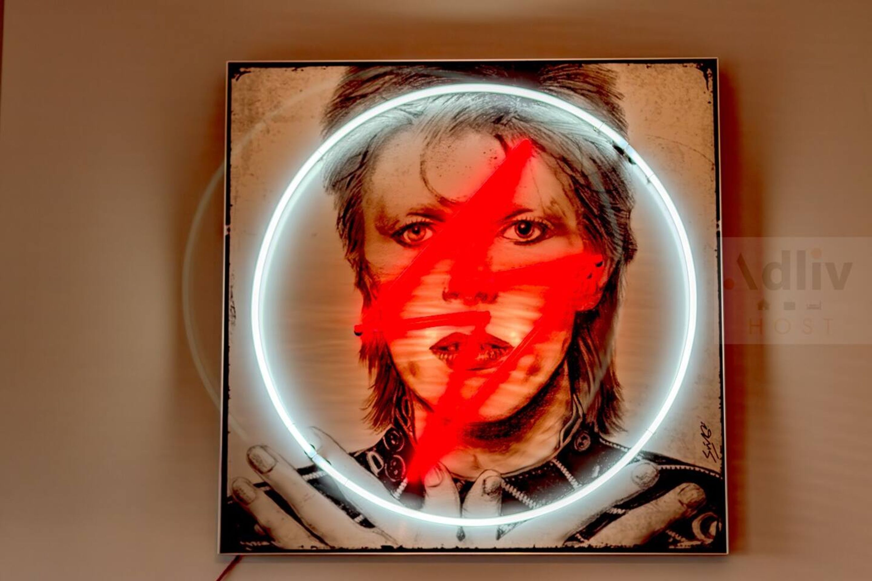 A framed artwork with a circular neon light effect, featuring a person with a blurred face and hands visible.