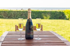 Eine Flasche Chapel Down English Sparkling Wine und zwei Gläser auf einem Holztisch, im Hintergrund Meer und Grünfläche.