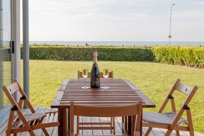 Une table en bois, deux chaises, une bouteille de vin et deux verres, le tout placé sur une terrasse offrant une vue sur la mer.