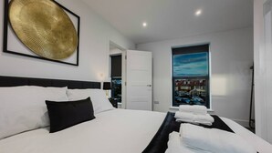 A modern hotel room with a large bed, a view of the city through a window, and a framed artwork on the wall. - Luxury Seaside Home Parking Sleeps 8 by Adliv (Margate)