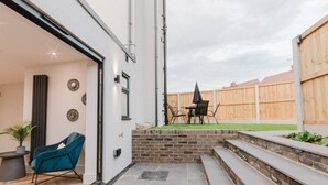A modern patio with a dining set, a brick wall, and a wooden fence in the background. - Luxury Seaside Home Parking Sleeps 8 by Adliv (Margate)