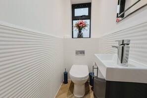 A modern bathroom with a white toilet, a sink, and a window with flowers.