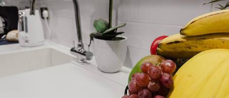 En vask med hane, en potteplante og en skål med bananer, druer og en melon.