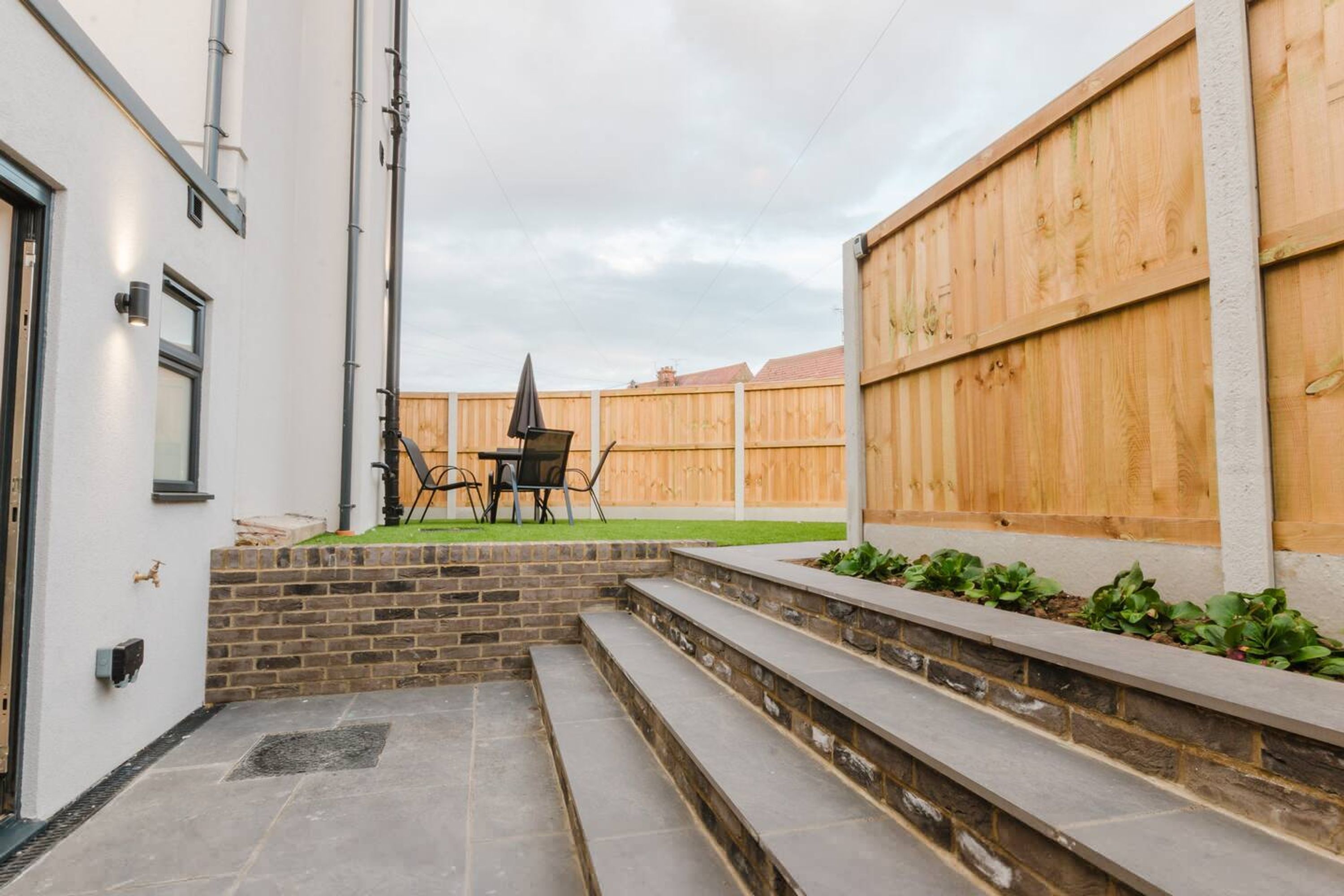A patio area with a stone bench, a table with chairs, and a wooden fence.