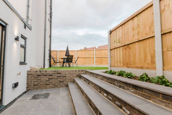 A patio area with a stone bench, a table with chairs, and a wooden fence.