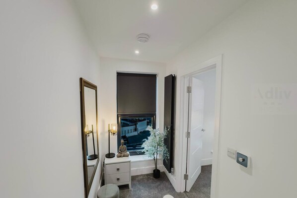 A narrow hallway with a window, a bedside table, a lamp, and a small potted plant. - Luxury Seaside Home Parking Sleeps 8 by Adliv (Margate)