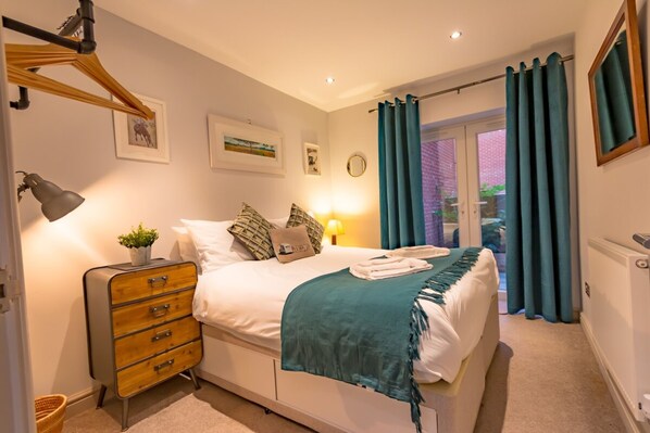 A neatly arranged bedroom with a bed, bedside lamp, dresser, and a view of the outdoors through a glass door.