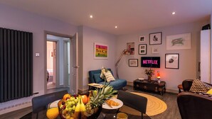 Ein modernes Wohnzimmer mit Essbereich, mit Obstschale, Couchtisch, Sofa und Fernseher, der 'NETFLIX' anzeigt.