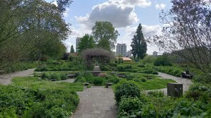Un jardín con un camino de piedra que conduce a un elemento central, rodeado de abundante vegetación y árboles.