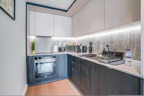 A modern kitchen with dark cabinetry, a built-in oven, a microwave, and a coffee maker. - Central London Stay in Vauxhall With Balcony (London)