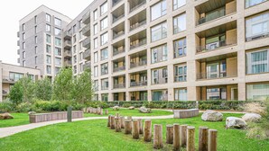 A multi-story residential building with balconies, a landscaped garden with grass and wooden posts, and a pathway. - Central London Stay in Vauxhall With Balcony (London)