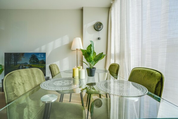 A modern dining area with a glass table, green chairs, candles, and a potted plant.