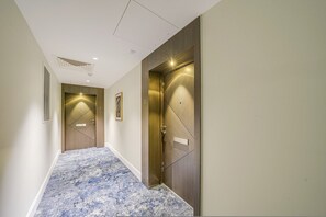 A hallway with a blue patterned carpet, two doors with illuminated panels, and a vent on the left wall. - Central London Stay in Vauxhall With Balcony (London)