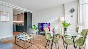 A modern living room with a glass dining table, green chairs, a flat-screen TV, and a kitchen in the background. - Central London Stay in Vauxhall With Balcony (London)