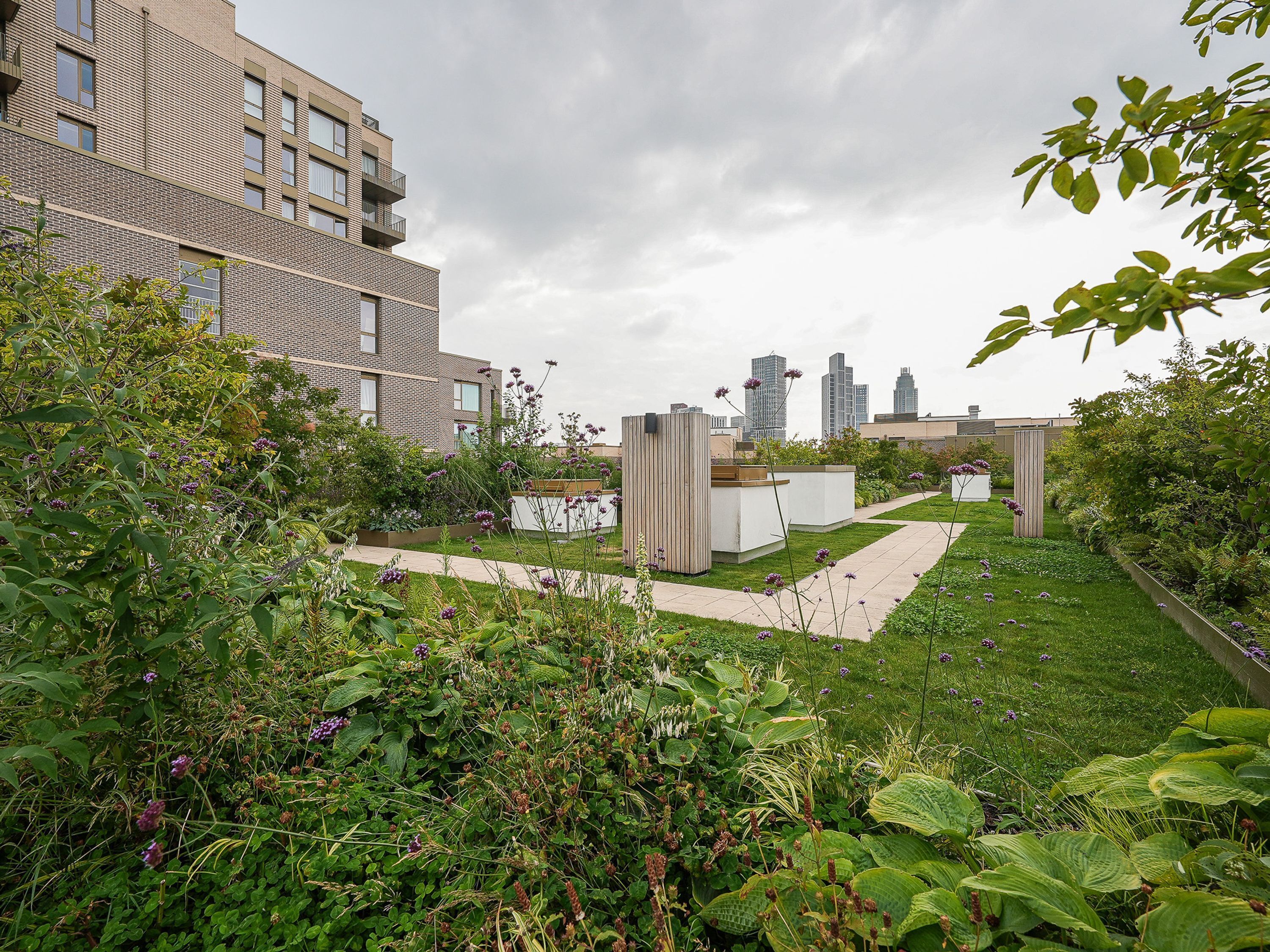 Un jardin sur le toit offrant une vue sur le paysage urbain, avec un bâtiment en briques, une structure blanche et diverses plantes.