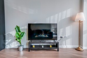 A modern living room with a flat-screen TV on a dark wooden stand, a potted plant, and a floor lamp. - Central London Stay in Vauxhall With Balcony (London)