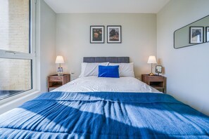 A bedroom with a bed, two nightstands, a window, and two framed pictures on the wall. - Central London Stay in Vauxhall With Balcony (London)