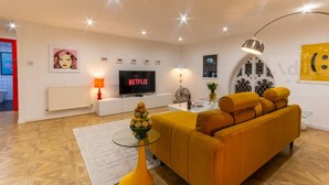 A modern living room with a sofa, a glass coffee table, a TV, and artwork on the walls.