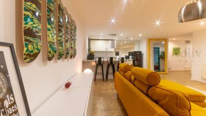 A modern living room with a yellow sofa, a white cabinet, and a kitchen in the background.