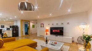 A modern living room with a sofa set, a coffee table, a TV, and a dining area with a refrigerator.