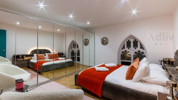 A modern bedroom with a large mirror, a bed with red and white bedding, a bedside table, and a chair.