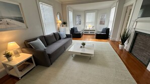 A modern living room with a grey sofa, white coffee table, and a fireplace. - Entire Charming Victorian Home Downtown Newport (Newport)