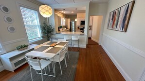 A modern kitchen with white cabinetry, a central island, and a dining area with a table and chairs. - Entire Charming Victorian Home Downtown Newport (Newport)