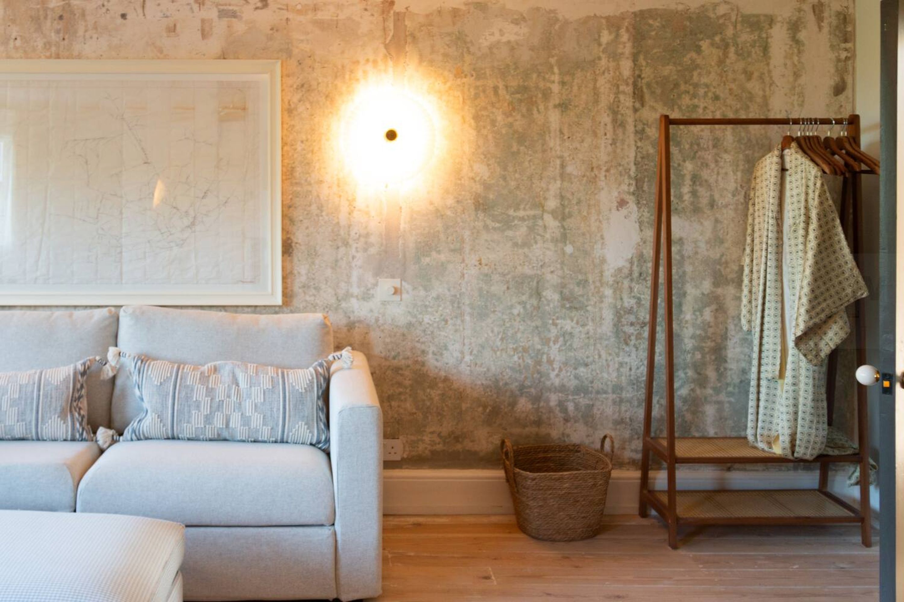 Ein Zimmer mit einem hellen Sofa, Holzboden, einer Karte an der Wand, einer Wandleuchte und einem Holzregal mit Kleidung.
