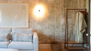 A room with a light-colored sofa, a wooden floor, a map on the wall, a wall-mounted light, and a wooden rack with clothes.