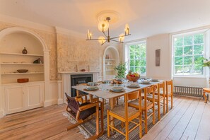 A dining room with a wooden table set for six, surrounded by chairs, a fireplace, and a large window with a view of trees. - Georgian Luxury Margate Tnhouse Sleeps 11 by Adliv (Margate)