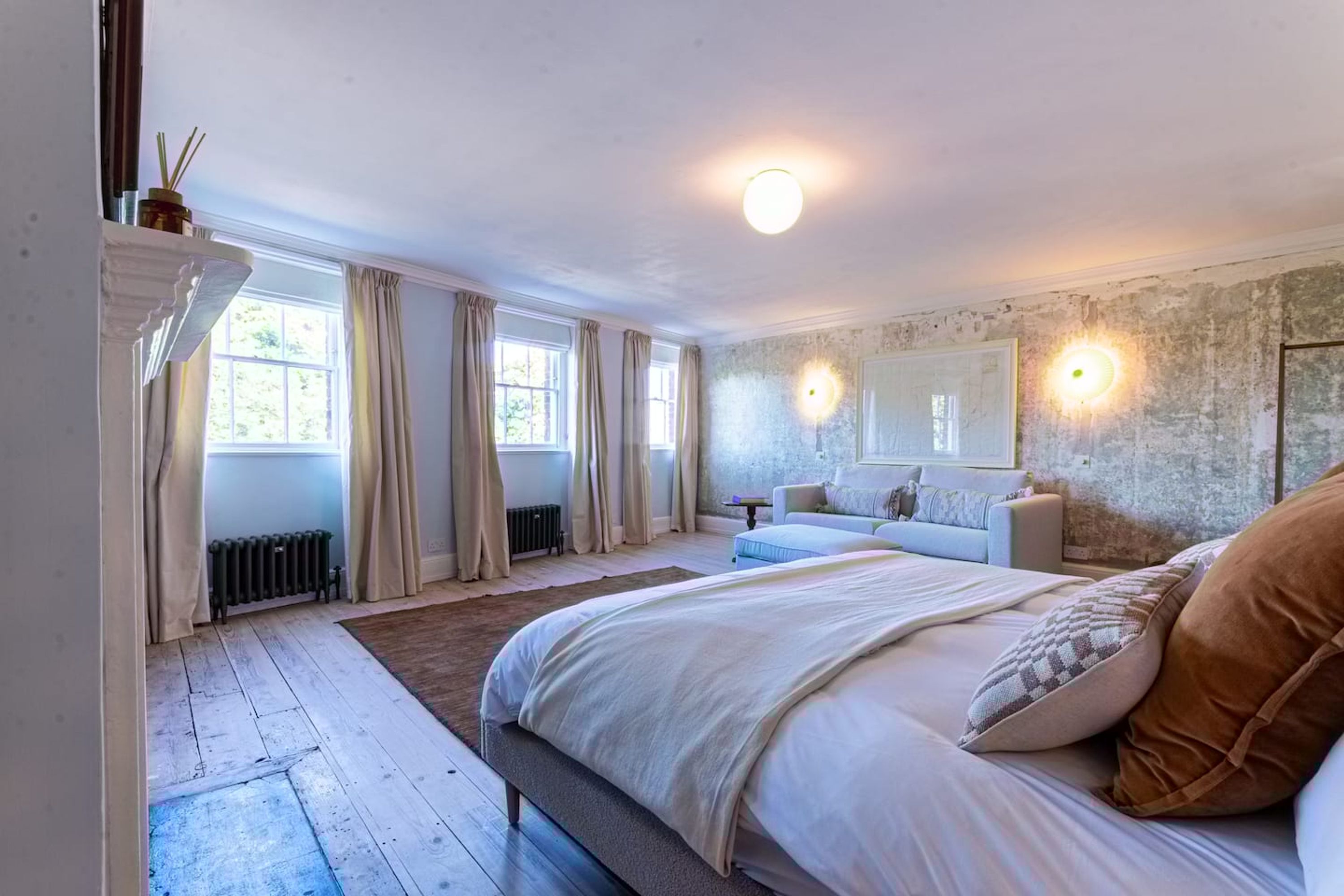 Ein Schlafzimmer mit einem großen Bett, einer Couch, einem Heizkörper und einem Fenster mit Vorhängen.