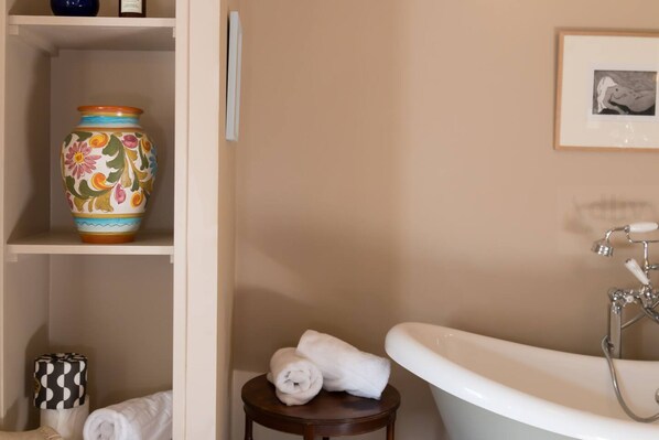 A bathroom with a bathtub, a shelf with a decorative vase, and a framed picture on the wall.