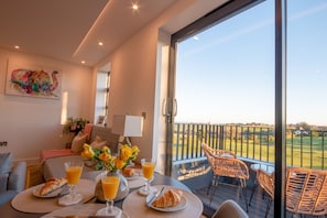 A balcony with breakfast setup including croissants, orange juice, and flowers.