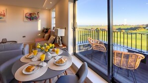 A dining area with a table set for breakfast, a balcony with wicker chairs, and a view of a golf course. - Luxury Ocean North Foreland Golf View By Adliv (Broadstairs)