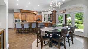 A spacious kitchen with wooden cabinets, a central island, and a dining area with a round table and chairs. - Private Riverbank 27-acre Estate 1 hr From Chicago (Kankakee)