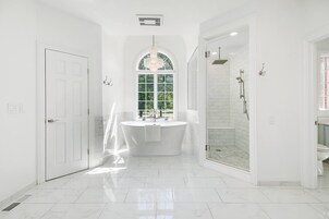 Un baño amplio con una bañera independiente, ducha a pie y un gran ventanal que proporciona luz natural.