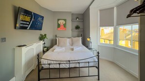 Ein Schlafzimmer mit Bett, Heizkörper, Fernseher, einem Gemälde, einem Fenster und Blick auf Gebäude.