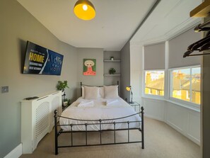 A bedroom with a bed, a radiator, a TV, a painting, a window, and a view of buildings outside. - Stunning Sea View Georgian Retreat by Adliv (Margate)