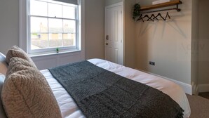 Un dormitorio con cama, ventana, puerta y un perchero para toallas.