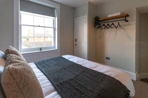 Un dormitorio con cama, ventana, puerta y un perchero para toallas.