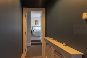 Un pasillo que conduce a un dormitorio con una cama, una mesita de noche y un cuadro en la pared.